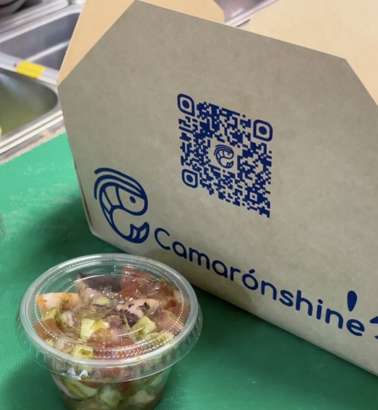 Kraft takeaway box printed with the logo and a QR code, next to a ceviche